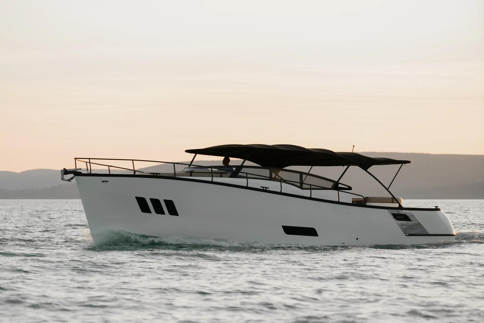 Die Wia 450 Cabrio mit weißem Rumpf und schwarzem Stoffverdeck bei Dämmerung auf dem Balaton, aus der Luft aufgenommen.