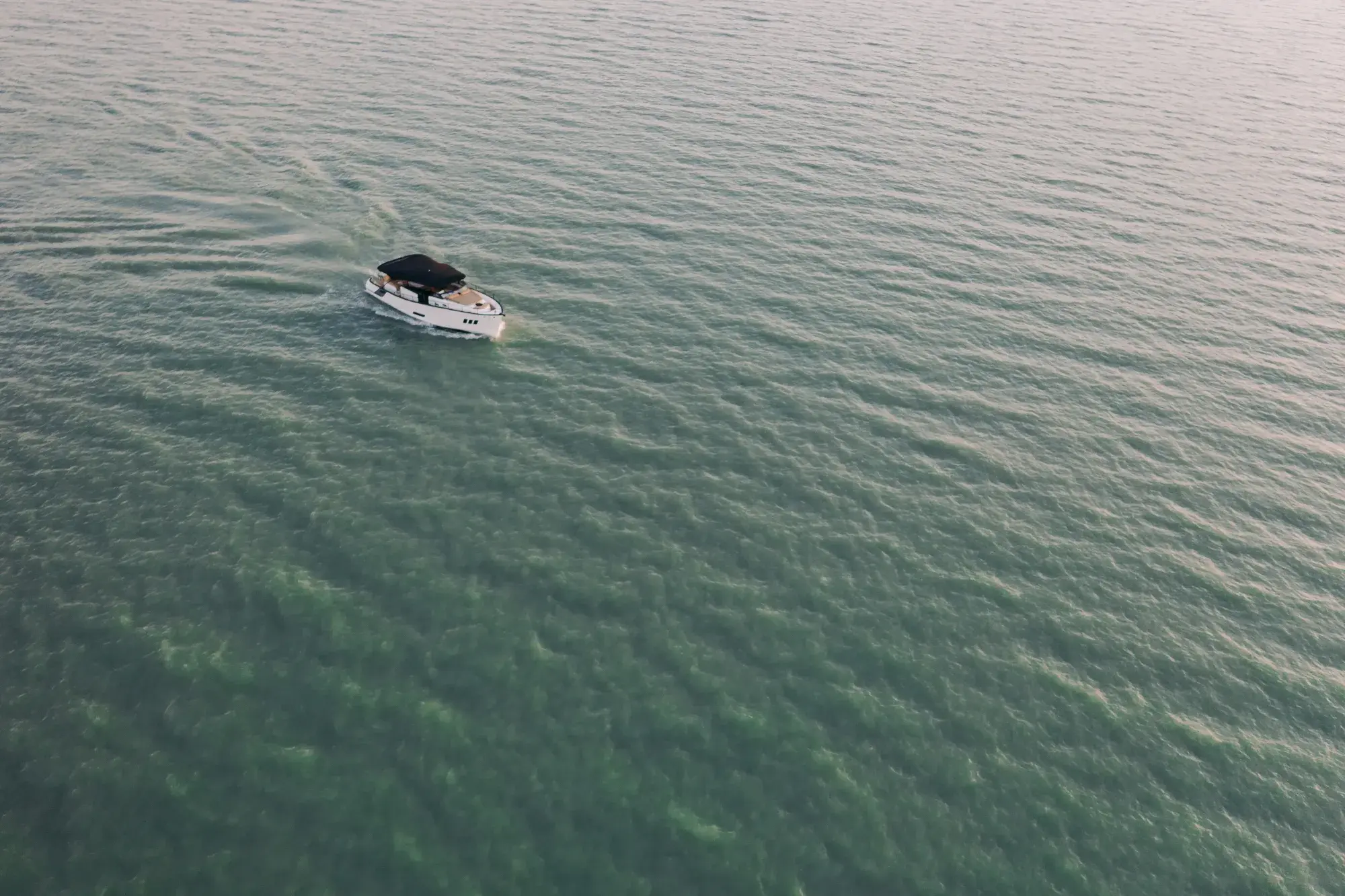 Die Wia 450 Cabrio aus großer Höhe auf schimmerndem grünem Wasser – ein kleines weißes Boot mit dunklem Verdeck, das eine feine Kielspur zieht.