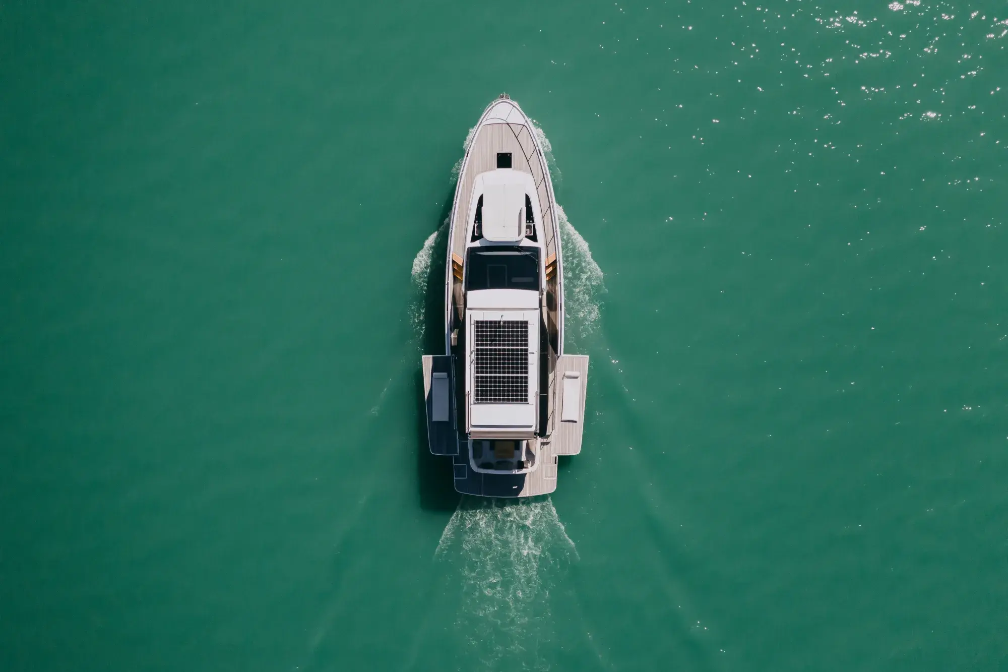La Wia 520 HardTop vue du dessus, son hardtop sombre à panneaux solaires, ses ponts en teck et son cockpit arrière ouvert sur l'eau verte.
