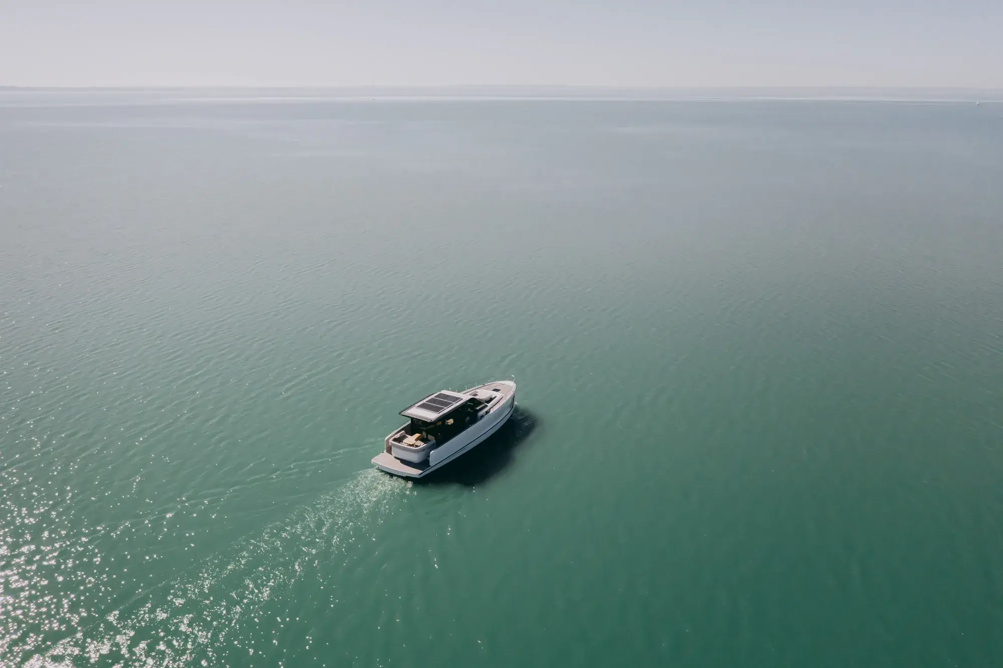 Die Wia 520 HardTop aus großer Höhe, ein weißer Cruiser mit dunklem Hardtop, der eine Kielspur über hinterleuchtetes grünes Wasser zieht.