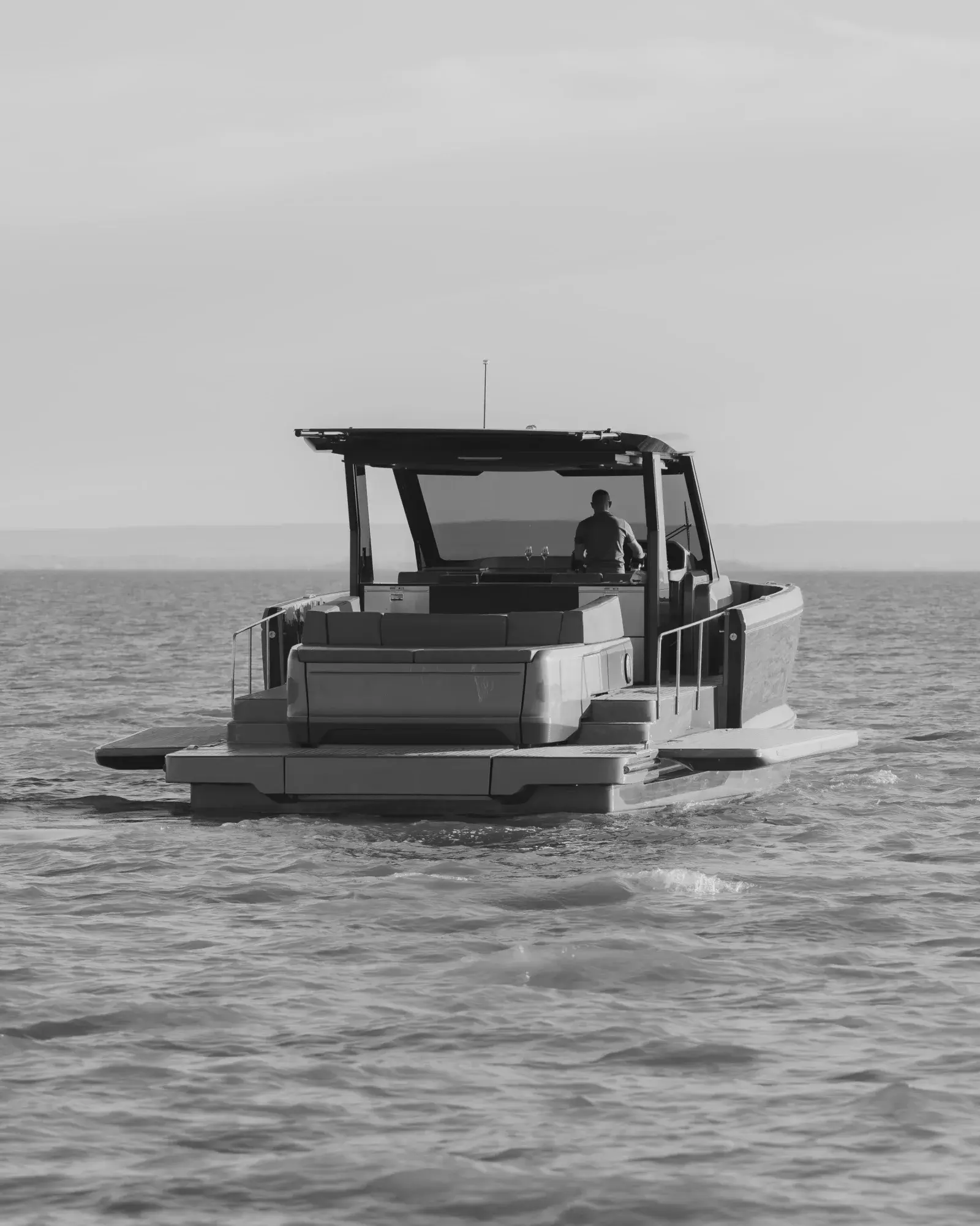 Schwarz-weiße Heckansicht einer Wia 520 Open, eine Person am Steuer unter dem offenen Hardtop, die Badeplattform knapp über dem Wasser.