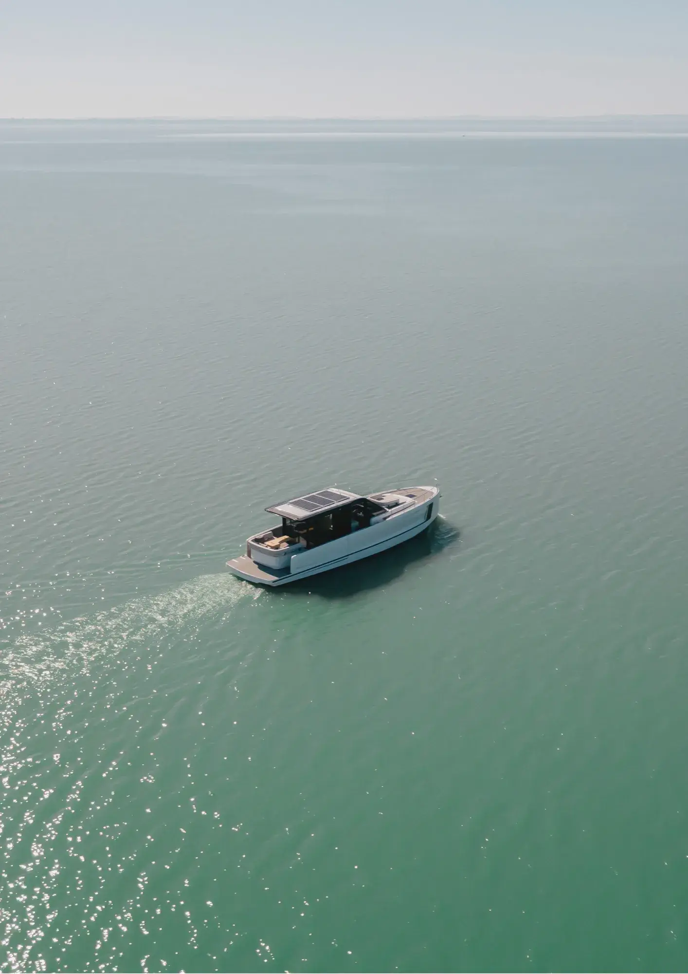 Aerial view of a white Wia yacht cruising alone across calm turquoise open water.