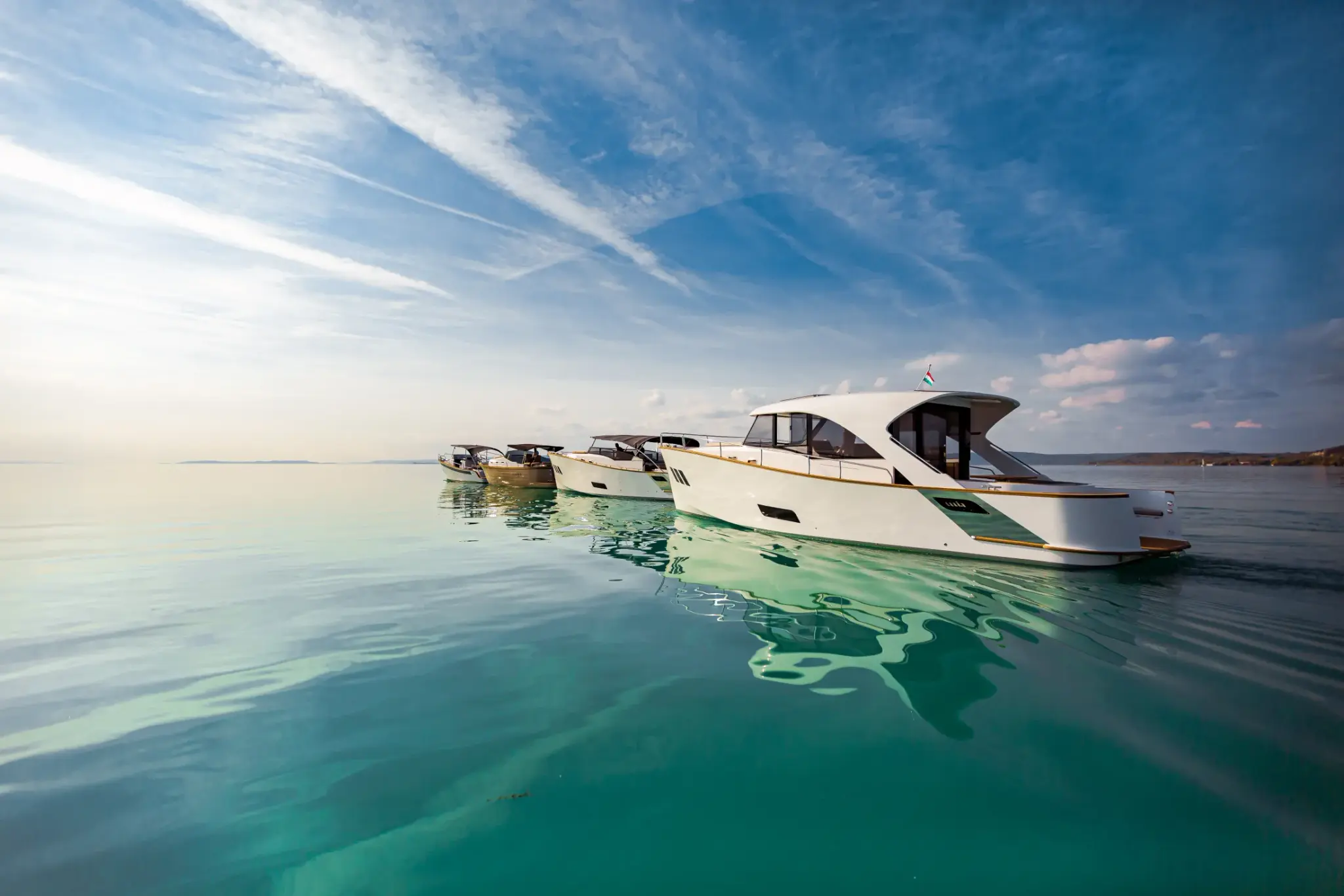 A row of Wia yachts on mirror-calm turquoise water at golden hour, their reflections below.
